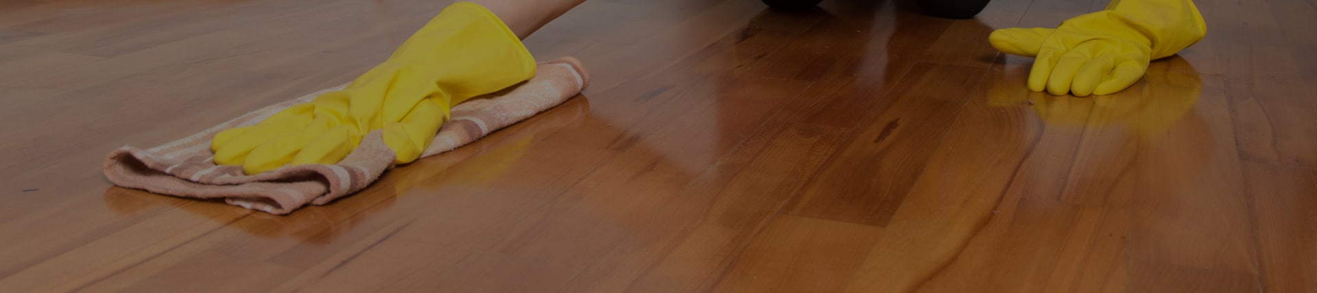 Pflege eines Holzbodens mit gelben Handschuhen und Putztuch