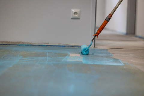 Nahaufnahme einer Malerrolle die eine blaue Grundierung auf den Fußboden aufträgt.