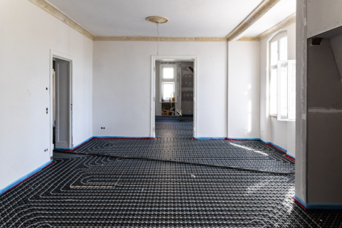 Unmöblierter Raum mit weißen Wänden und sichtbarer Fußbodenheizung, die mit den angrenzenden Räumen verbunden ist; durch die Fenster fällt Sonnenlicht ein.