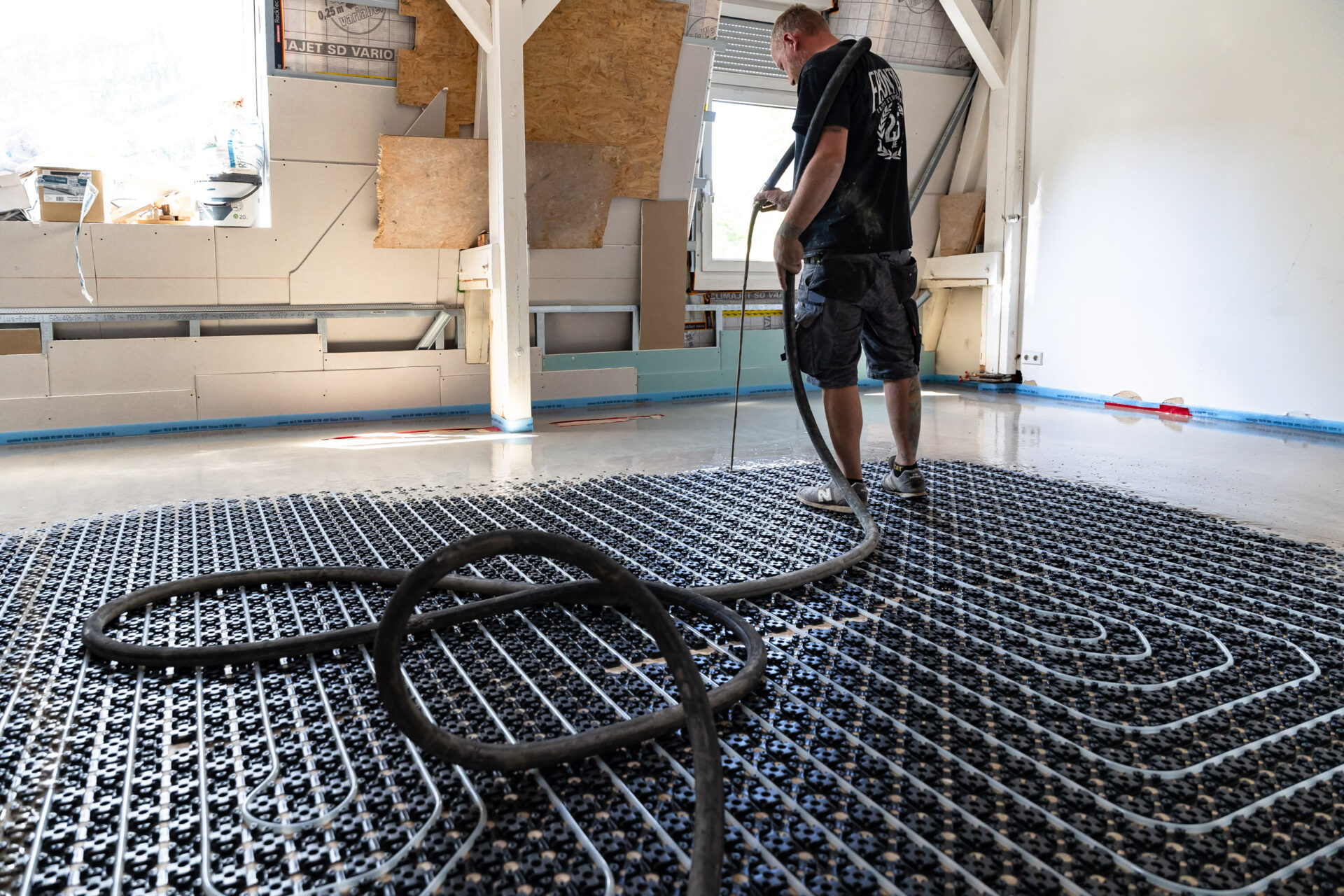 Ein Arbeiter gießt während eines Bau- oder Renovierungsprojekts in einem Gebäude Beton über Fußbodenheizungsrohre.