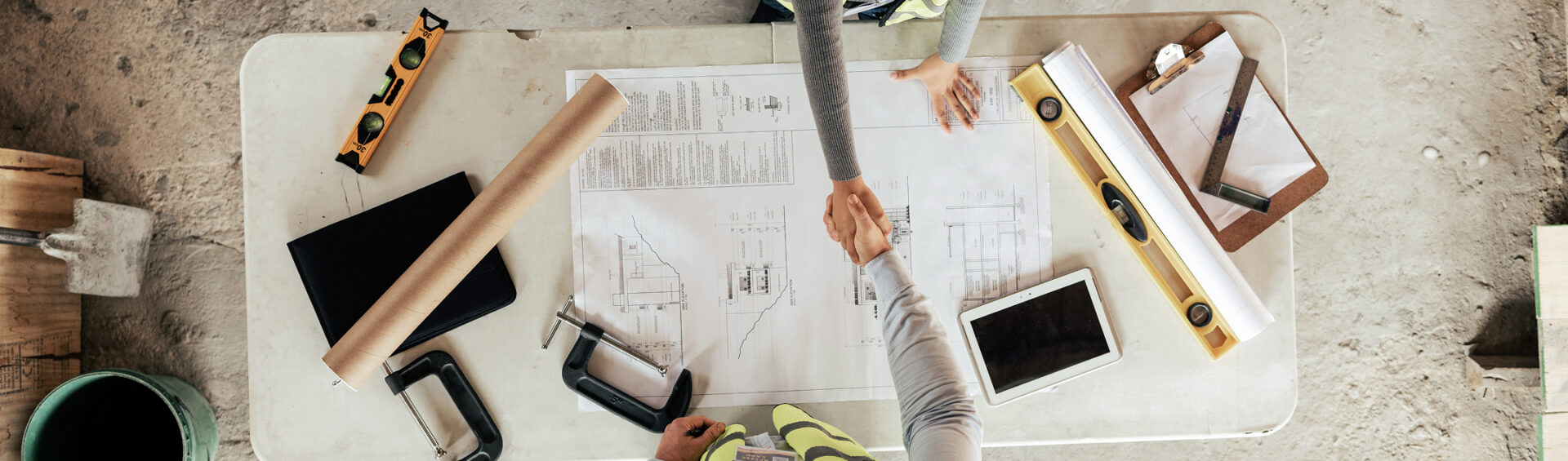 Architekt und Bauherr geben sich über einem Bauplan die Hand – Symbol für erfolgreiche Zusammenarbeit auf der Baustelle.