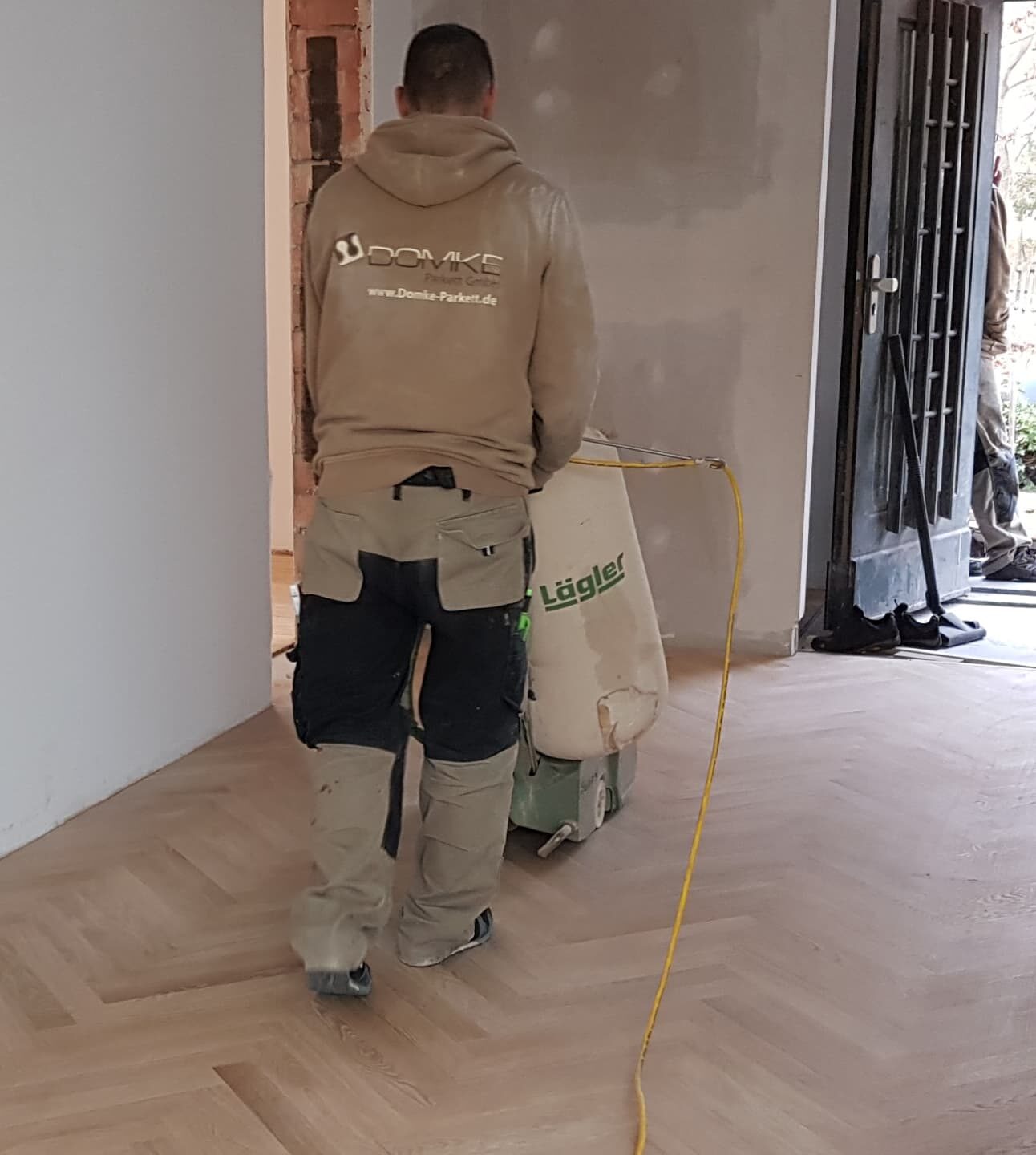 Mitarbeiter der Domke Parkett GmbH Berlin schleift Parkettboden mit professioneller Maschine im Wohnbereich ab – präzise Handwerksarbeit für hochwertige Bodensanierung