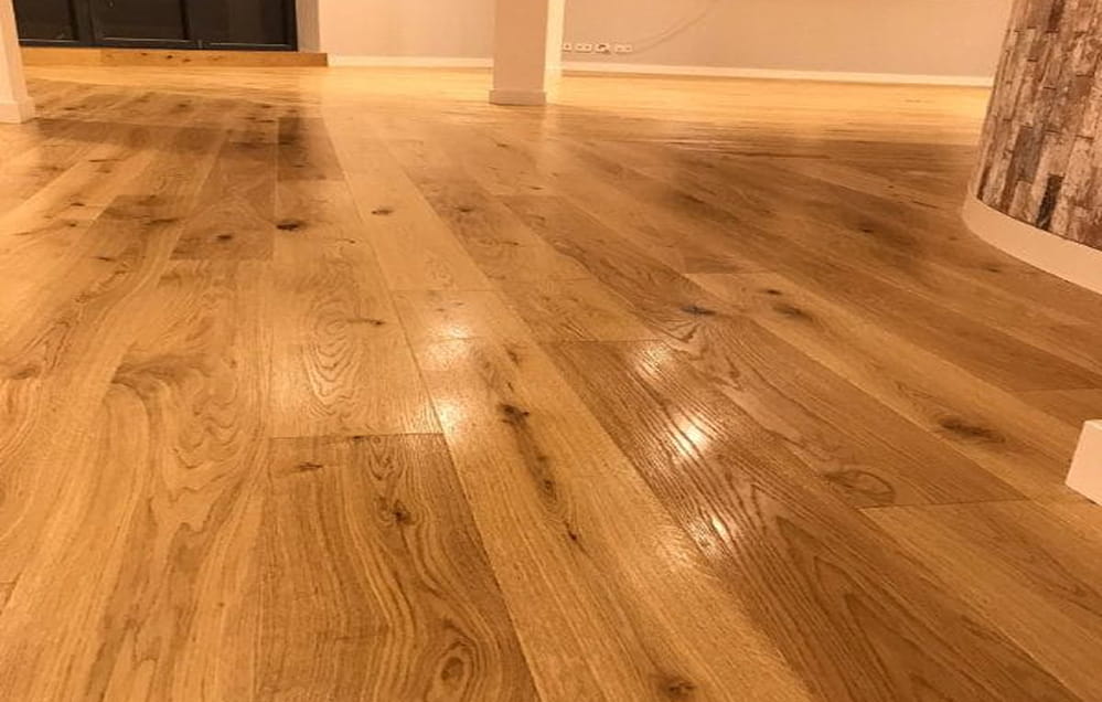 Ein Raum mit hellbraunem Dielenboden mit glatter Oberfläche und sichtbaren Holzmaserungen; weiße Wände und Säulen sind teilweise sichtbar.