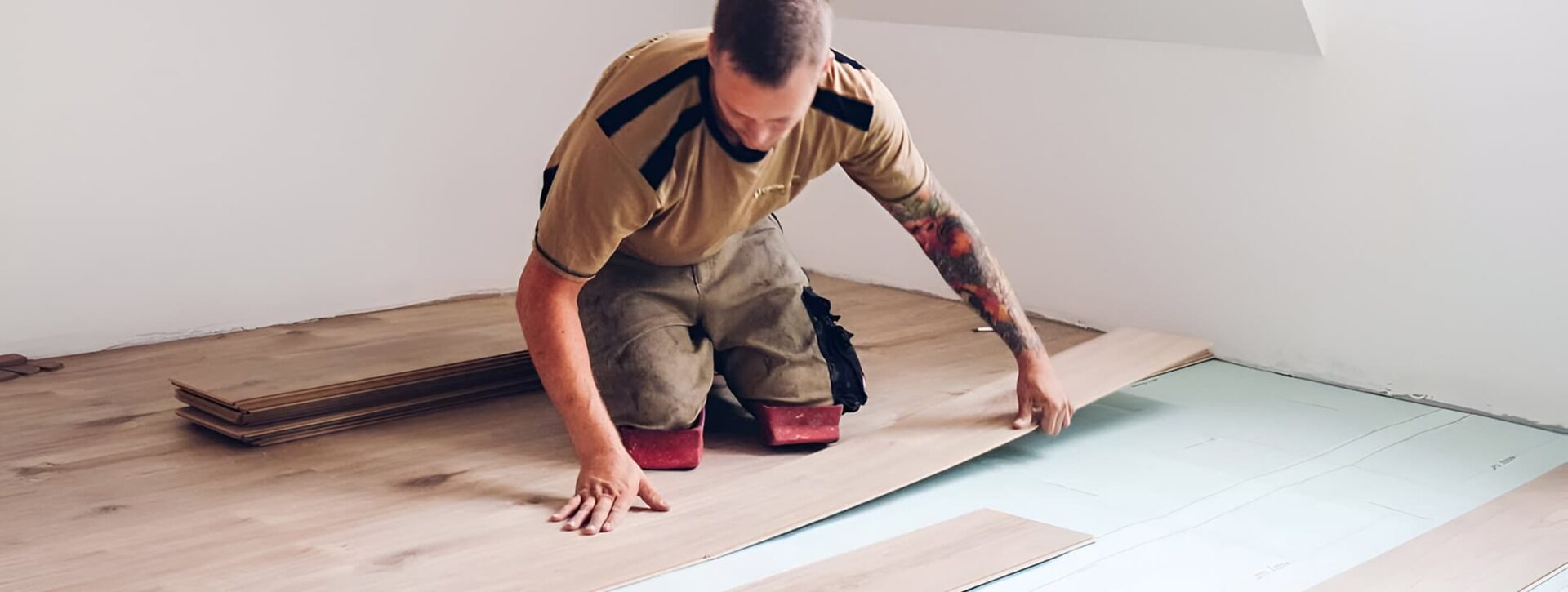 Handwerker verlegt helle Parkettdielen in einem Dachgeschossraum auf Trittschalldämmung.