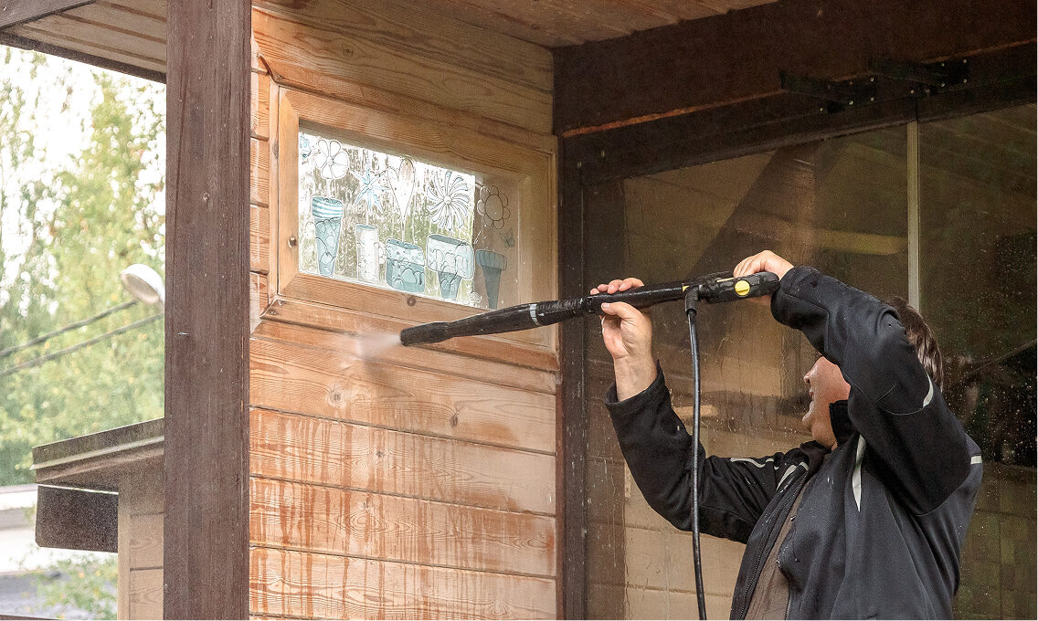 Reinigung einer Holzfassade mit Hochdruckreiniger unterhalb eines kleinen Fensters.
