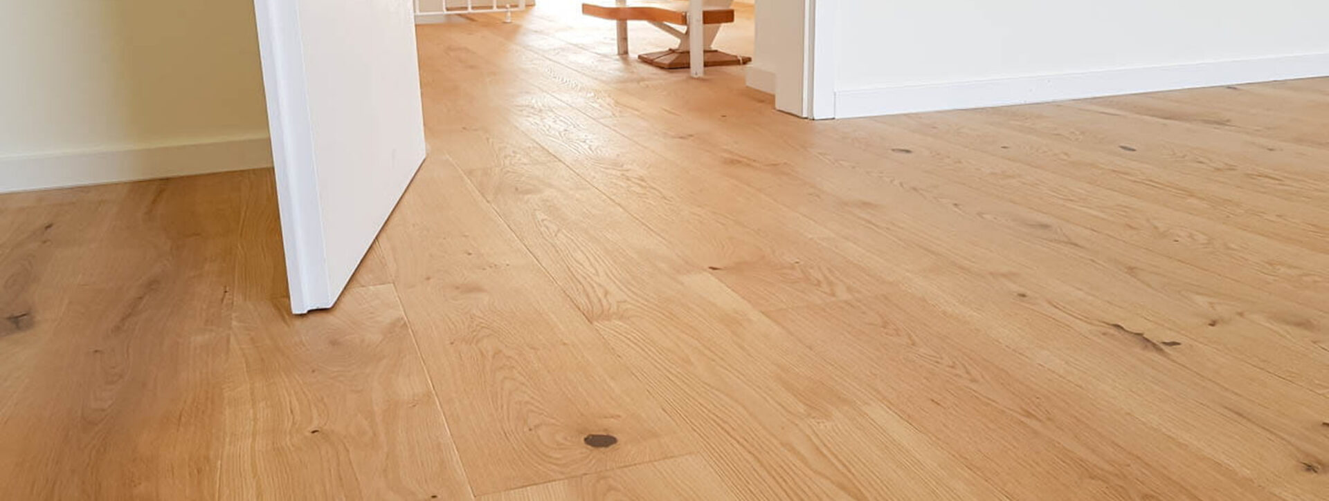 Heller Eichenparkettboden frisch verlegt in einem modernen Wohnraum mit geöffneter Tür und Blick in den Flur.