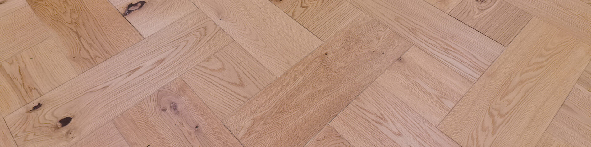 Nahaufnahme eines hochwertigen Fischgrät-Parkettbodens aus Eichenholz mit natürlicher Maserung und Astlöchern.