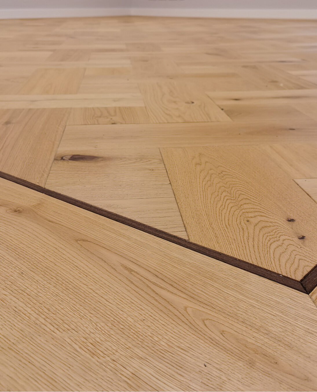 Detailansicht eines Fischgrät-Parkettbodens mit umlaufender dunkler Holzintarsie.