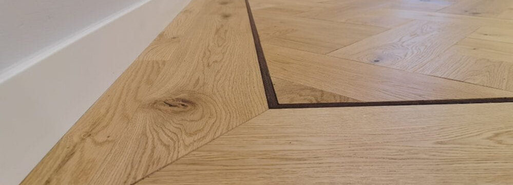 Nahaufnahme eines professionell verlegten Flechtparketts mit sauber gearbeiteten Rändern und dunkler Randumrahmung.