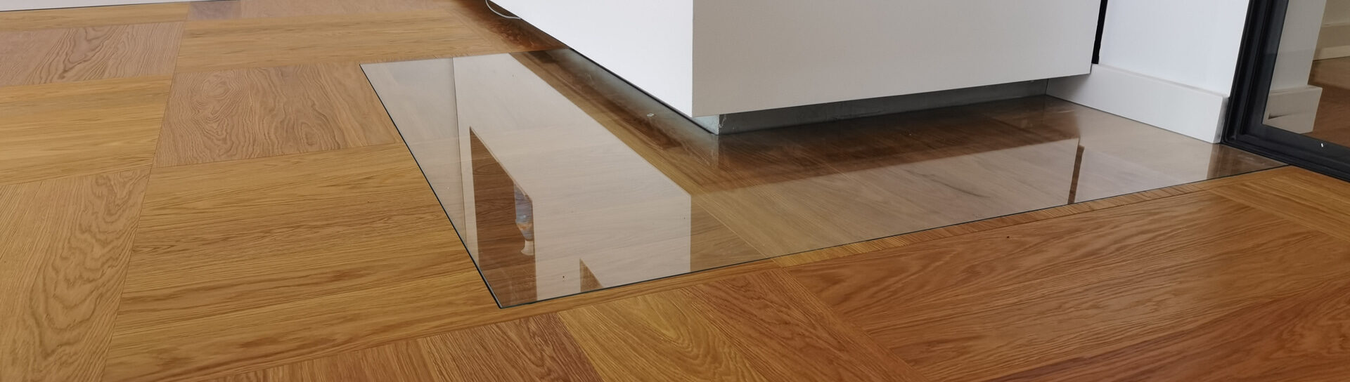 eingelassene Funkenschutzplatte aus Glas vor einem Kamin im modernen Wohnraum mit Parkettboden.