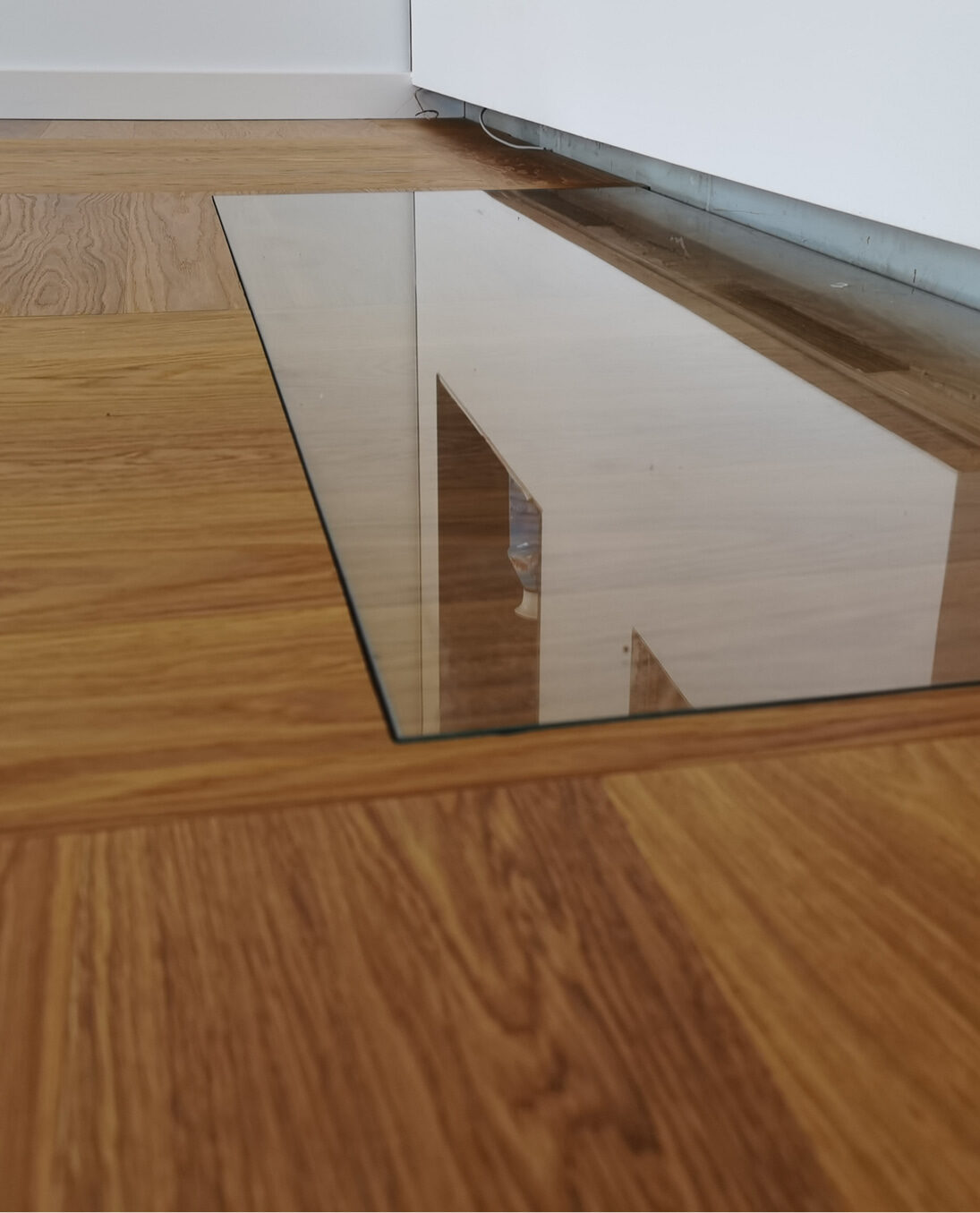 Funkenschutzplatte aus Glas flächenbündig in Eichenparkett eingelassen, Seitenansicht mit klarer Kantenführung und moderner Integration.