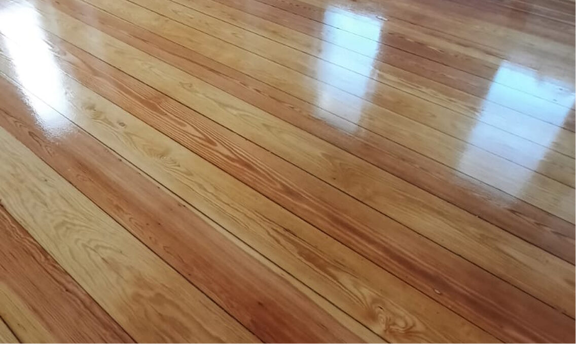 Frisch geschliffener und glänzend versiegelter Holzboden mit sichtbarer Holzmaserung und Spiegelung von Fenstern.
