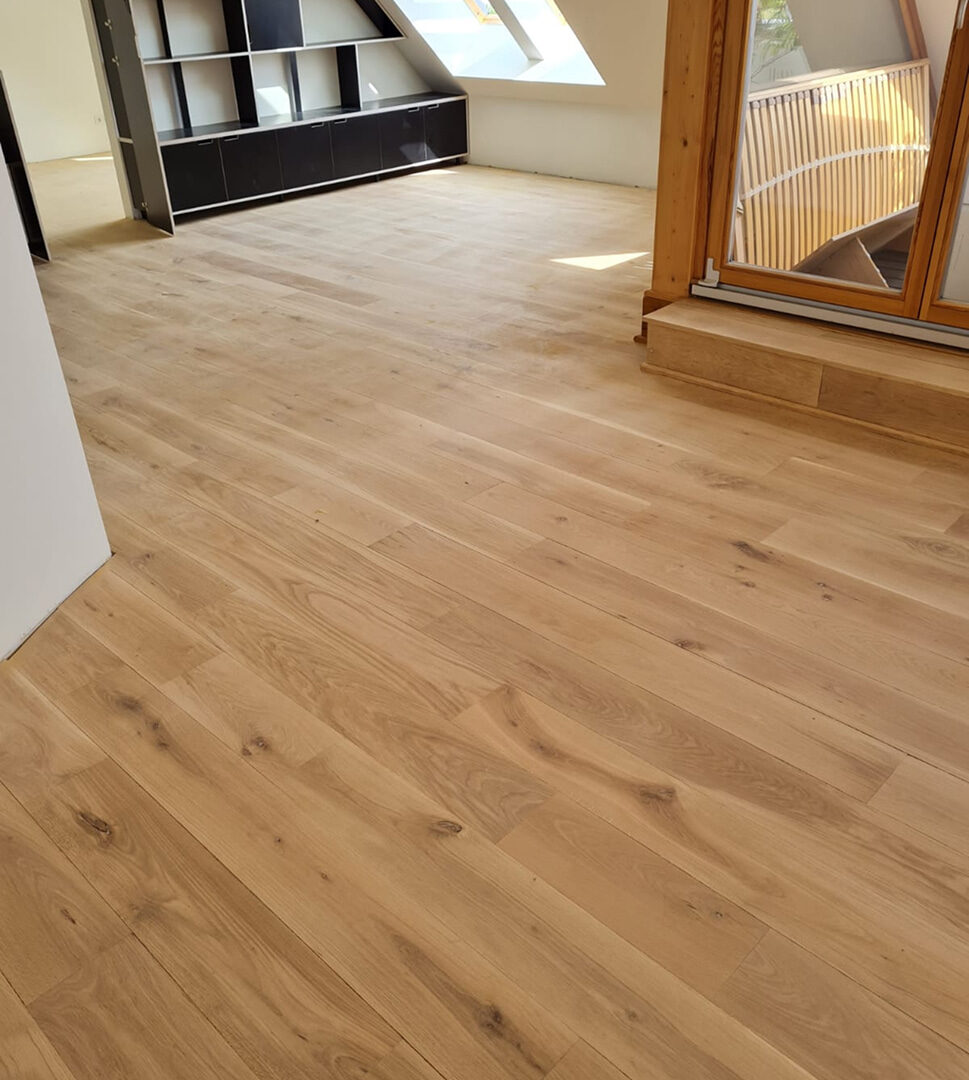 Heller Laminatboden in einem modernen Dachgeschoss mit Einbauschränken und großen Fenstern.