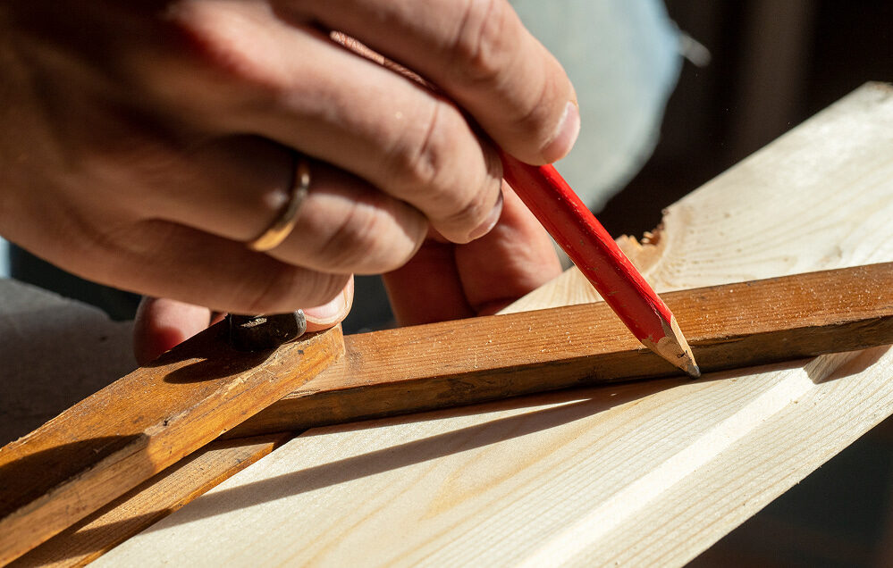 Hand markiert mit einem Bleistift eine präzise Linie auf einem Holzbrett zur Vorbereitung für den Zuschnitt.