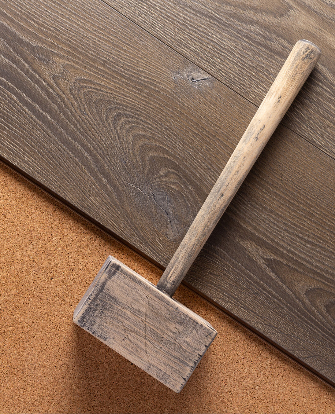 Ein traditioneller Holzhammer liegt auf dunklem Parkettboden mit Korkunterlage – Werkzeug für die fachgerechte Verlegung von Holzböden.