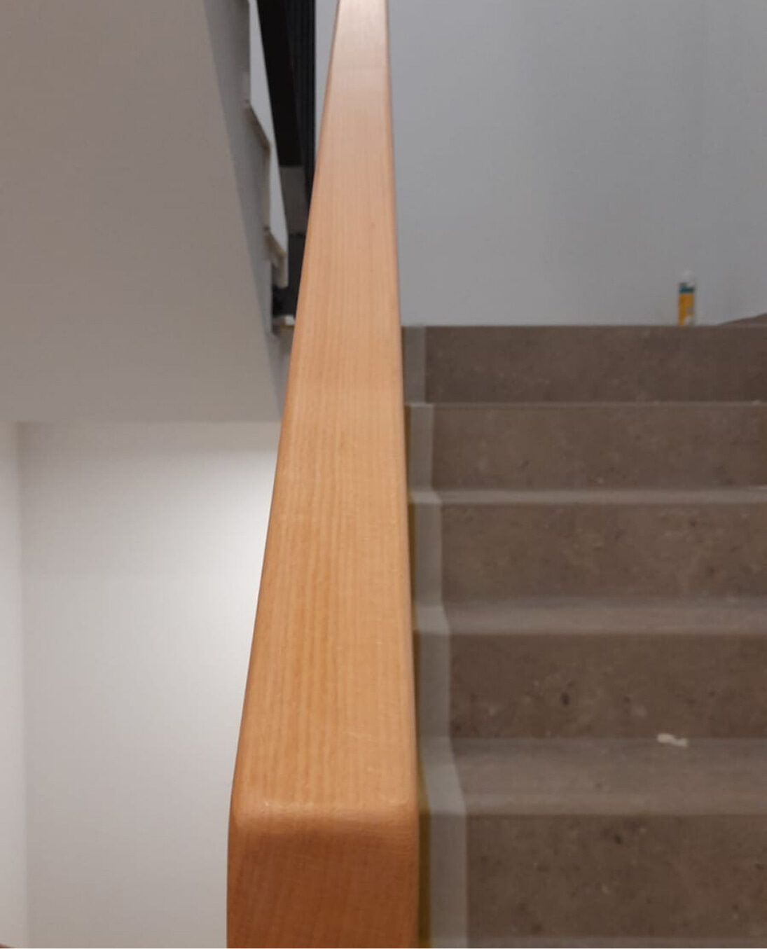Massiver Holzhandlauf an einer Betontreppe, frontal fotografiert in moderner Innenarchitektur.