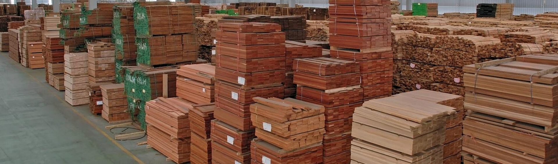 Große Lagerhalle mit gestapeltem Holz in verschiedenen Ausführungen – veranschaulicht die aktuelle Marktsituation mit Materialengpässen und zeigt die Bevorratungslösung von Domke Parkett zur Absicherung von Verfügbarkeit und Preis.