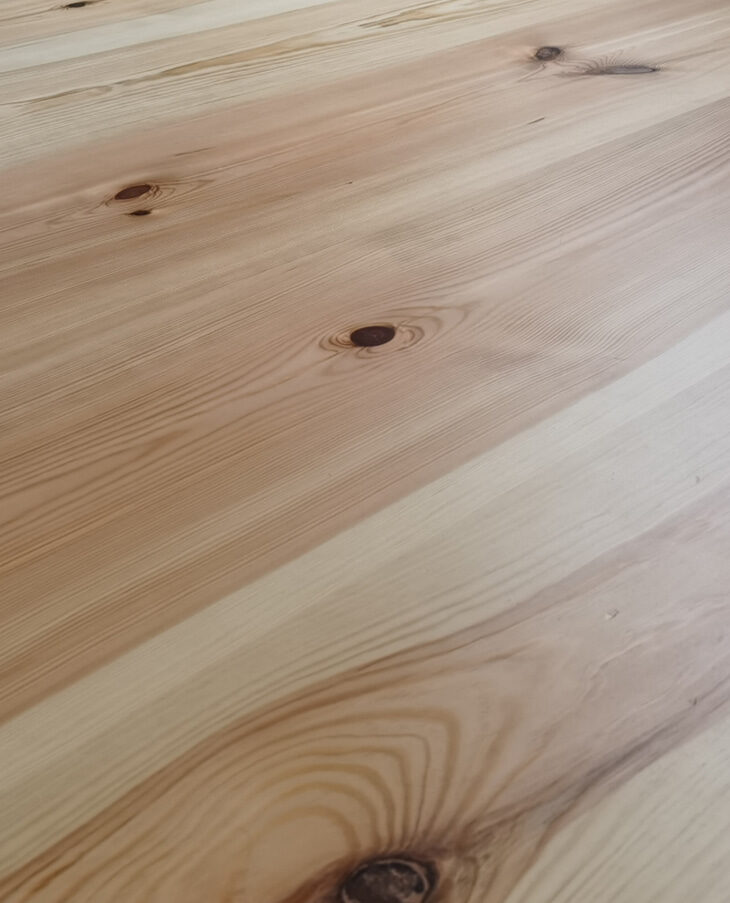 Nahaufnahme eines Holzbodens mit markanten Aststellen und gut sichtbarer Maserung in warmen Naturtönen.