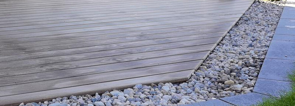 Holzterrasse mit schräg verlegten Dielen und dekorativem Kiesrand zur Abgrenzung.