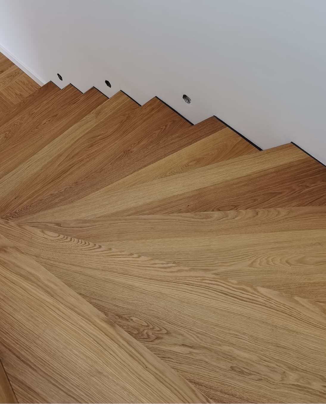 Detailaufnahme einer modern gestalteten Holztreppe aus Eiche mit fächerförmiger Stufenanordnung.