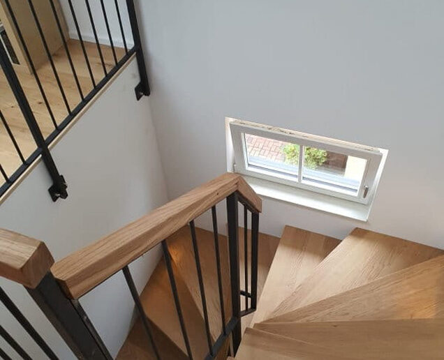 Holztreppe mit schwarzem Metallgeländer und Fenster im modernen Innenraum.