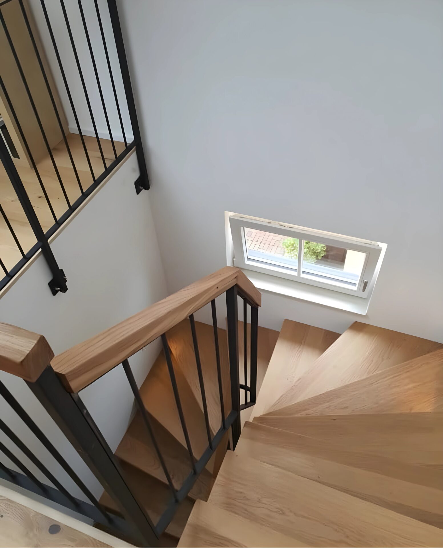 Moderne Holztreppe mit massiven Eichenstufen und schwarzem Metallgeländer in einem hellen Treppenhaus.