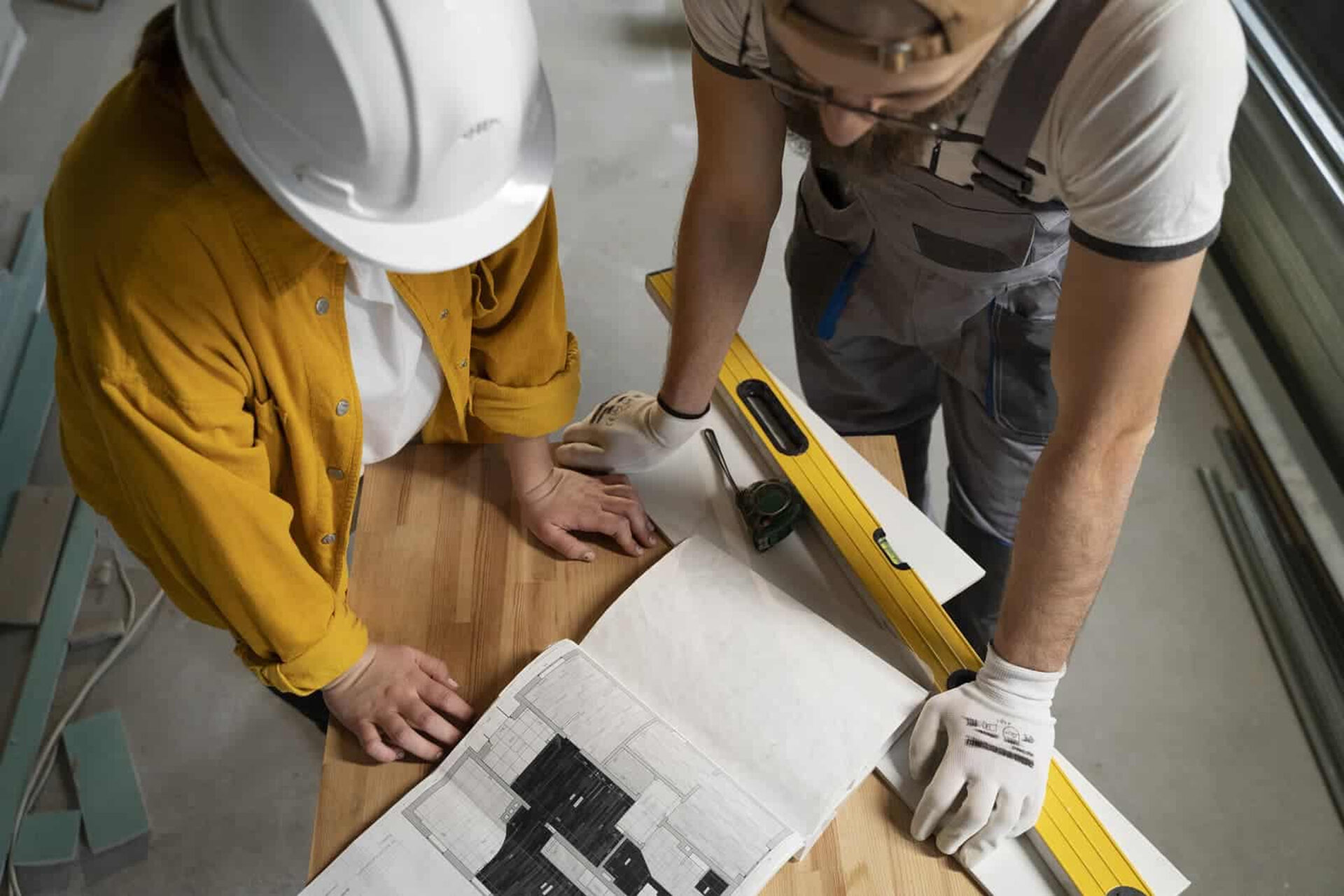 Zwei Fachkräfte mit Bauplan, Wasserwaage und Maßband bei der Projektbesprechung – Symbolbild für die verantwortungsvolle Arbeit als Projektleiter im Bereich Türen bei Domke Parkett GmbH.