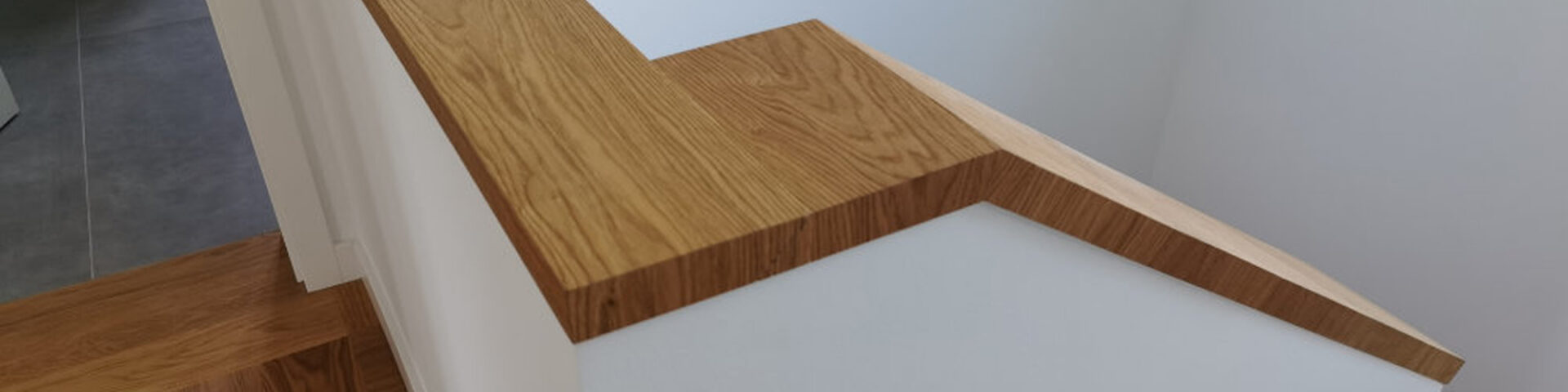 Massivholz-Handlauf auf weißem Treppengeländer mit präziser Gehrung – moderne und hochwertige Innenarchitektur mit natürlichem Holzfinish.
