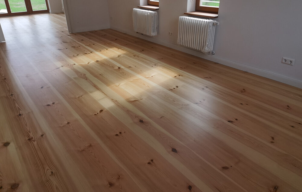 Massivholzdielen raumlang im lichtdurchfluteten Wohnbereich mit Heizkörpern.