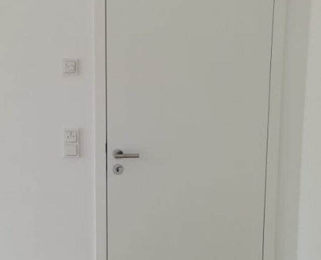 Schlicht designte weiße Innentür mit silberner Türklinke in modernem Wohnraum.