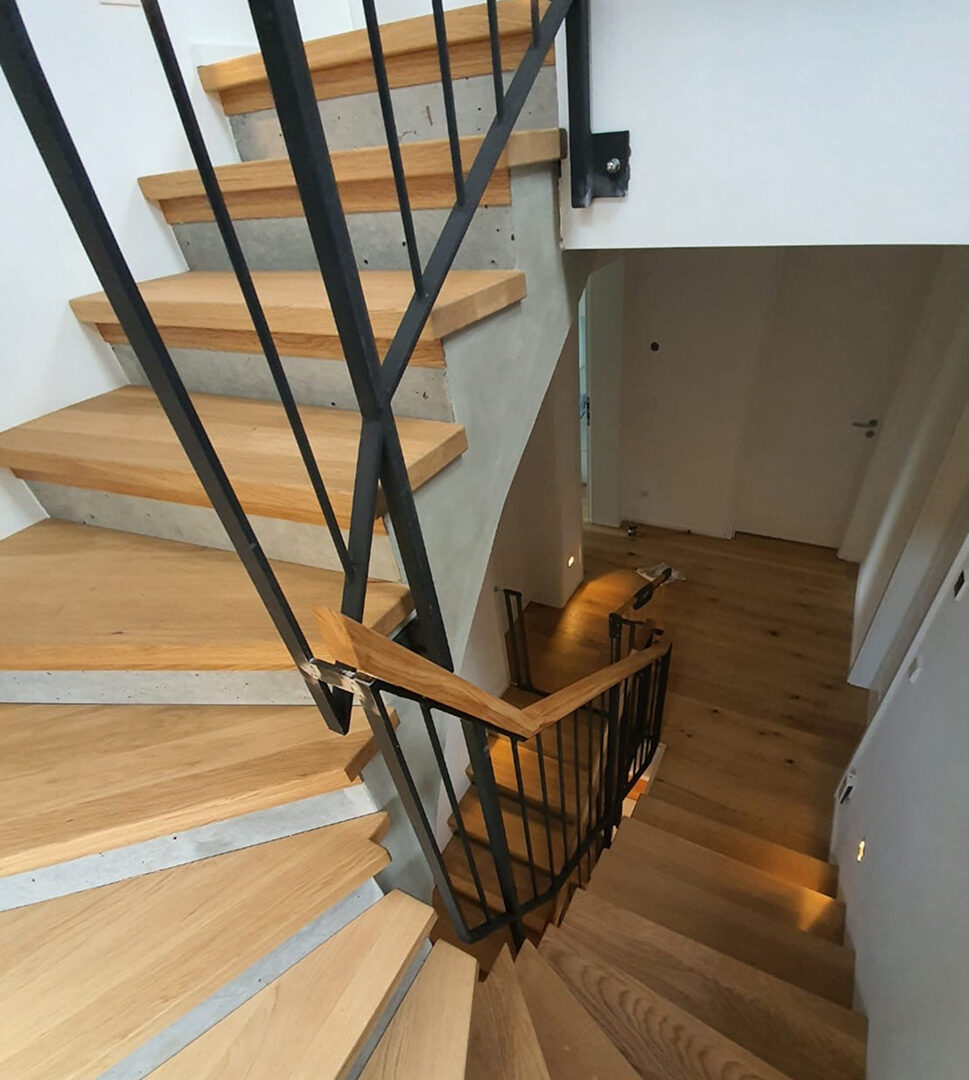 Moderne Holztreppe mit schwarzen Metallgeländern in einem hellen Innenraum, mit Eichenstufen und integriertem Handlauf aus Holz.