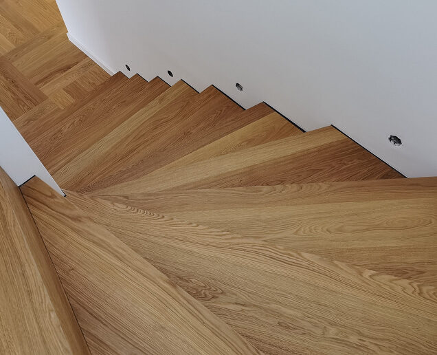 Detailansicht einer modern verkleideten Holztreppe mit durchgehender Maserung und weißer Wand.