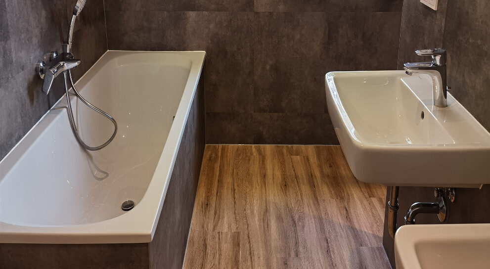 modernes Badezimmer mit Badewanne und Waschbecken auf Holzoptikboden.