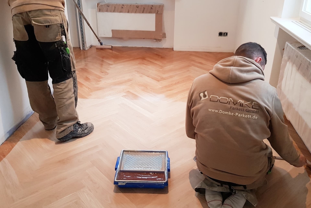 Parkettleger beim Ölen eines frisch verlegten Fischgrätparketts, mit Farbrolle und Lackwanne, Domke Parkett GmbH bei der Bodenbearbeitung im Innenraum