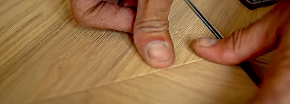 Detailaufnahme einer Hand, die eine Parkettverbindung exakt ausrichtet – präzises Arbeiten beim Verlegen eines Holzfußbodens.