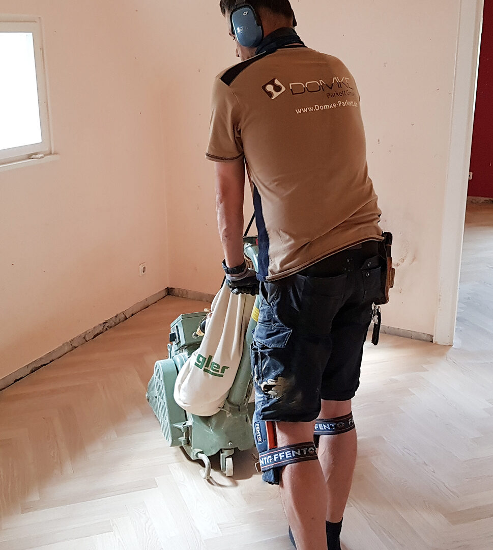 Mitarbeiter von Domke Parkett beim Abschleifen eines Parkettbodens mit einer professionellen Schleifmaschine.