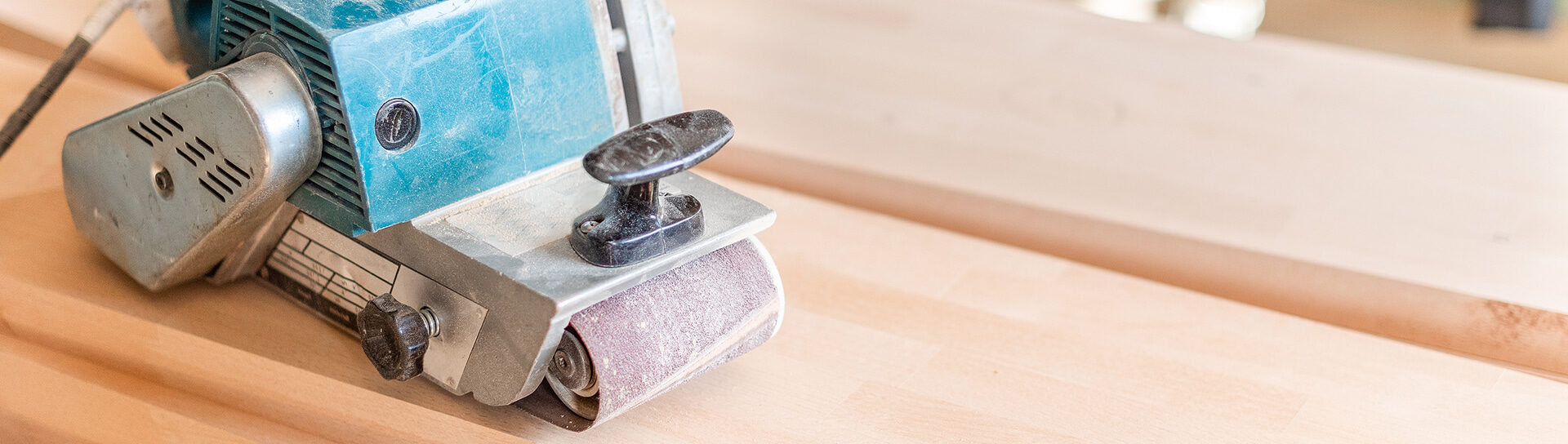 Detailaufnahme einer elektrischen Schleifmaschine auf einem hellen Holzfußboden während der Parkettrenovierung.