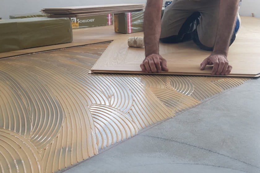 Bei der Verlegung von Holzfußböden werden die Dielen über einen Kleber verlegt, der auf eine Betonfläche aufgetragen wird.