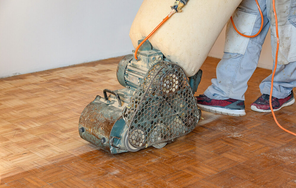 Eine Schleifmaschine schleift einen neue verlegten Parkettboden.