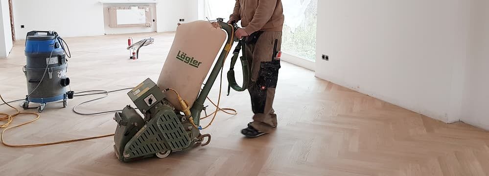 Mitarbeiter der Domke Parkett GmbH Berlin schleift Fischgrätparkett mit professioneller Lägler-Maschine – fachgerechte Renovierung für edle Holzböden