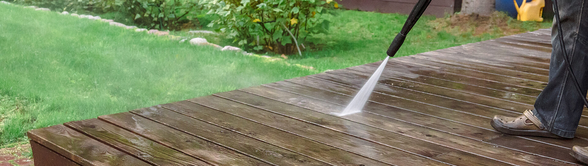 Reinigung einer Holzterrasse mit einem Hochdruckreiniger im Garten.