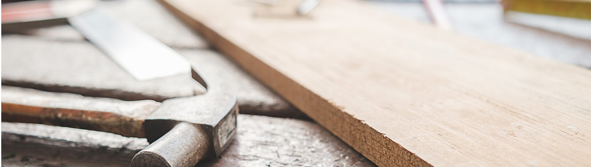 Nahaufnahme einer Holzplatte mit Hammer und Säge auf einer Werkbank – Symbolbild für präzise Tischlerarbeiten und handwerkliches Arbeiten mit Holz.