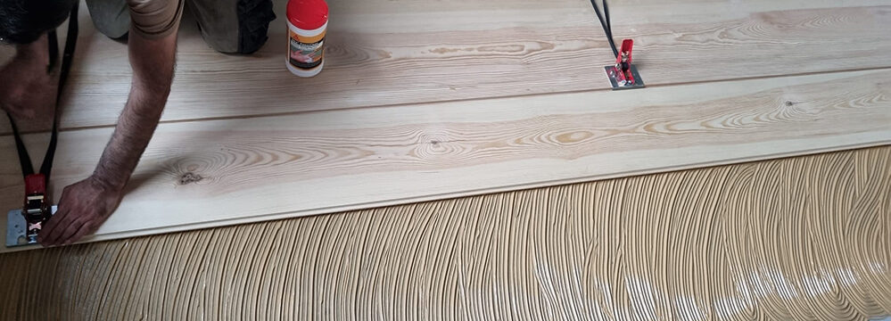 Handwerker verklebt raumlange Dielen auf vorbereitetem Untergrund.