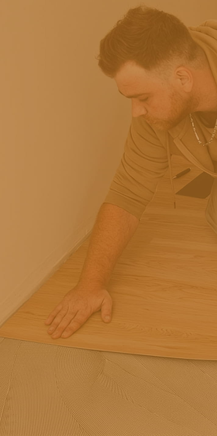 Ein Mitarbeiter von Domke Parkett verklebt Vinylstreifen fachgerecht auf dem Fußboden. Das Bild ist rötlich eingefärbt.