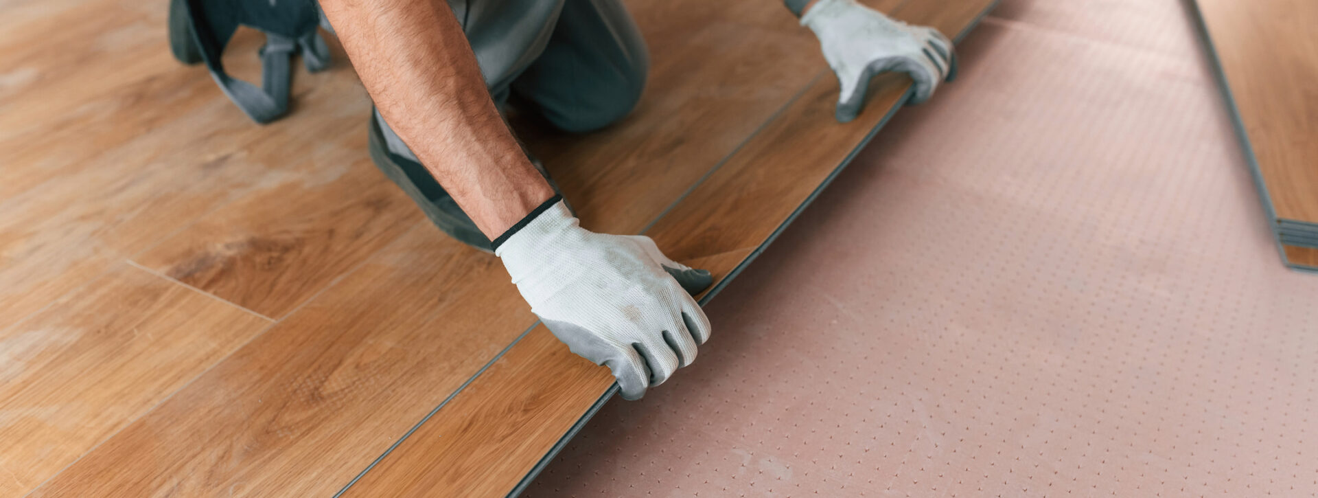 Handwerker verlegt Vinylboden auf rosa Trittschalldämmung mit präziser Klickverbindung.