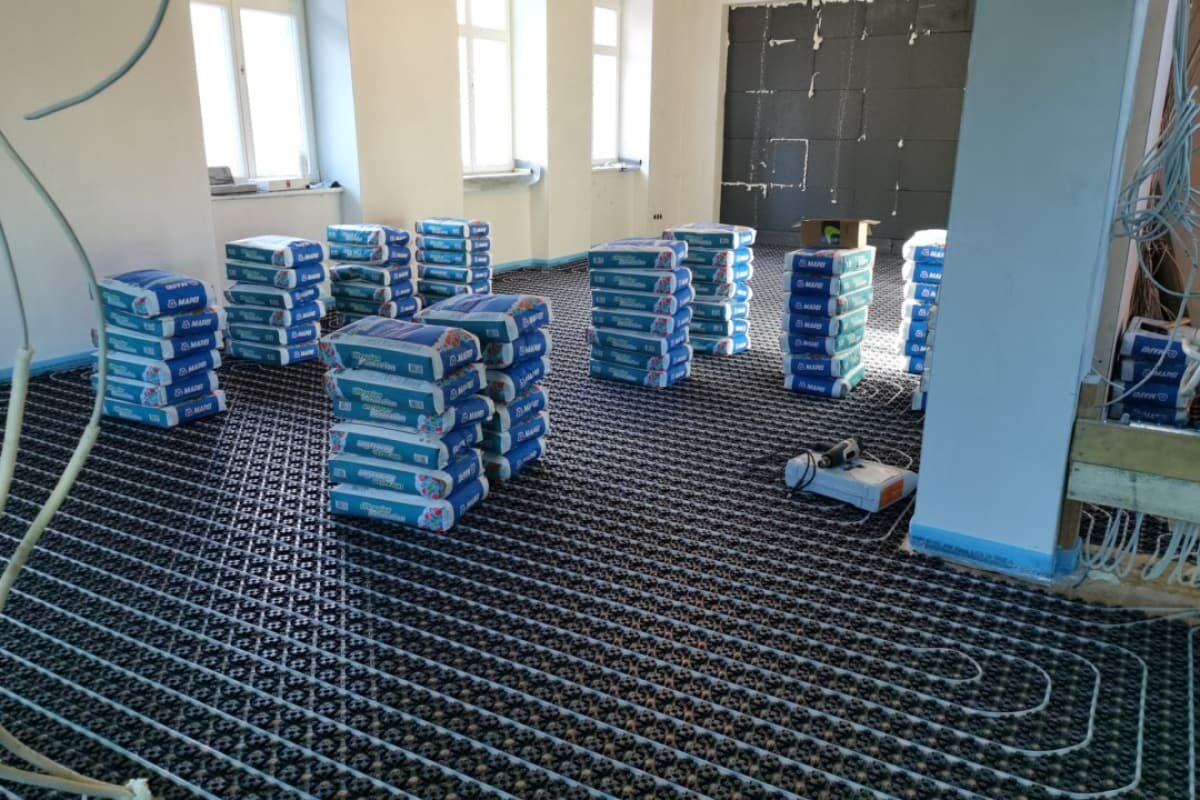 Vorbereitete Fläche mit installierter Fußbodenheizung und gestapeltem Material für Estrichverlegung in Altbauräumen.