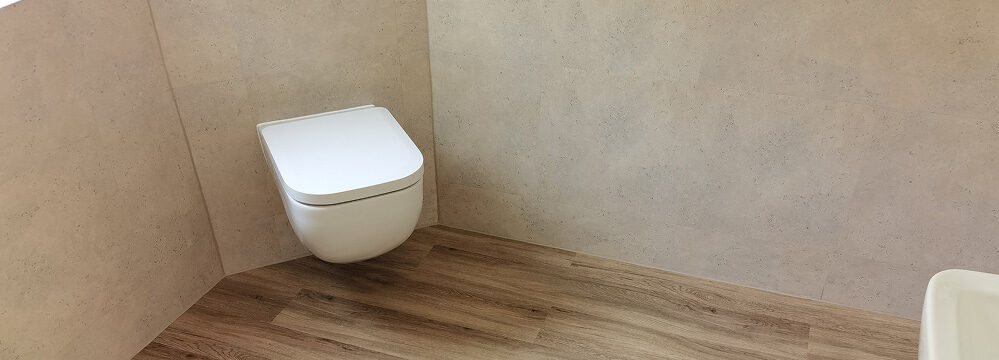 wandhängendes WC mit heller Wandverkleidung und Holzoptikboden.