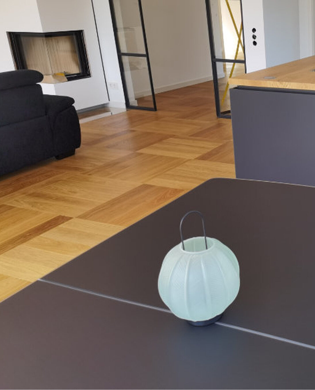 wohnzimmer mit modernem Würfelparkettboden und schwarzem Sofa im Hintergrund.